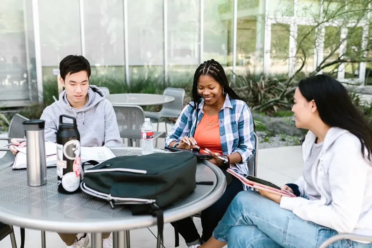 Three students comparing study options with tablets and notes at a campus table