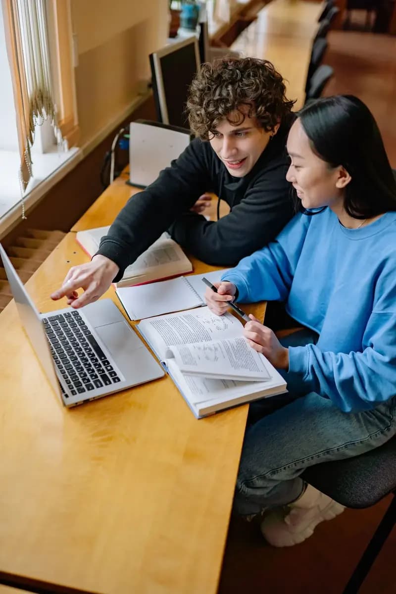 Two students comparing options on a laptop in a library
